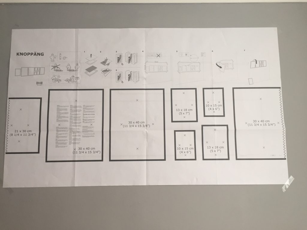 Grey wall covered with a paper template containing black boxes and instructions on how to hang the photoframes