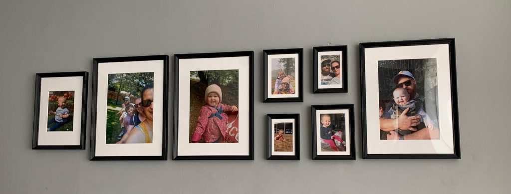 Eight black photoframes on a grey wall all of containing family photographs