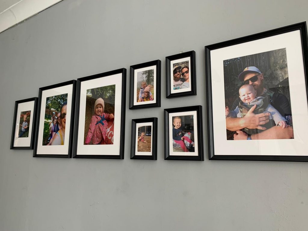 Eight black photoframes on a grey wall all of containing family photographs